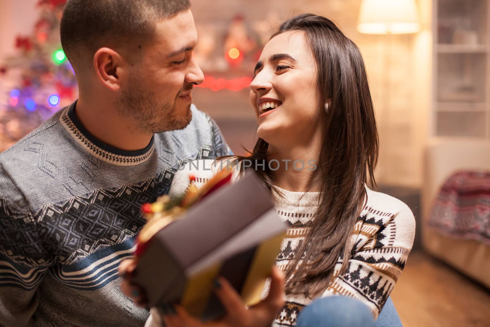 Smiling couple looking at each other on christmas day. Girl with gift box.