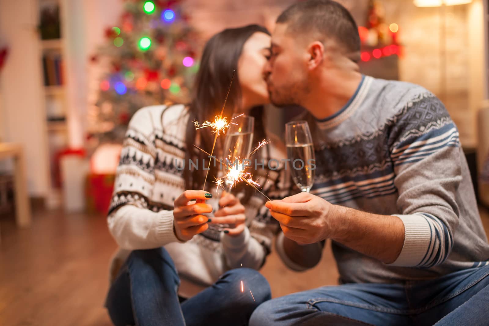 Couple holding burning sparkles on christmas day while kissing.