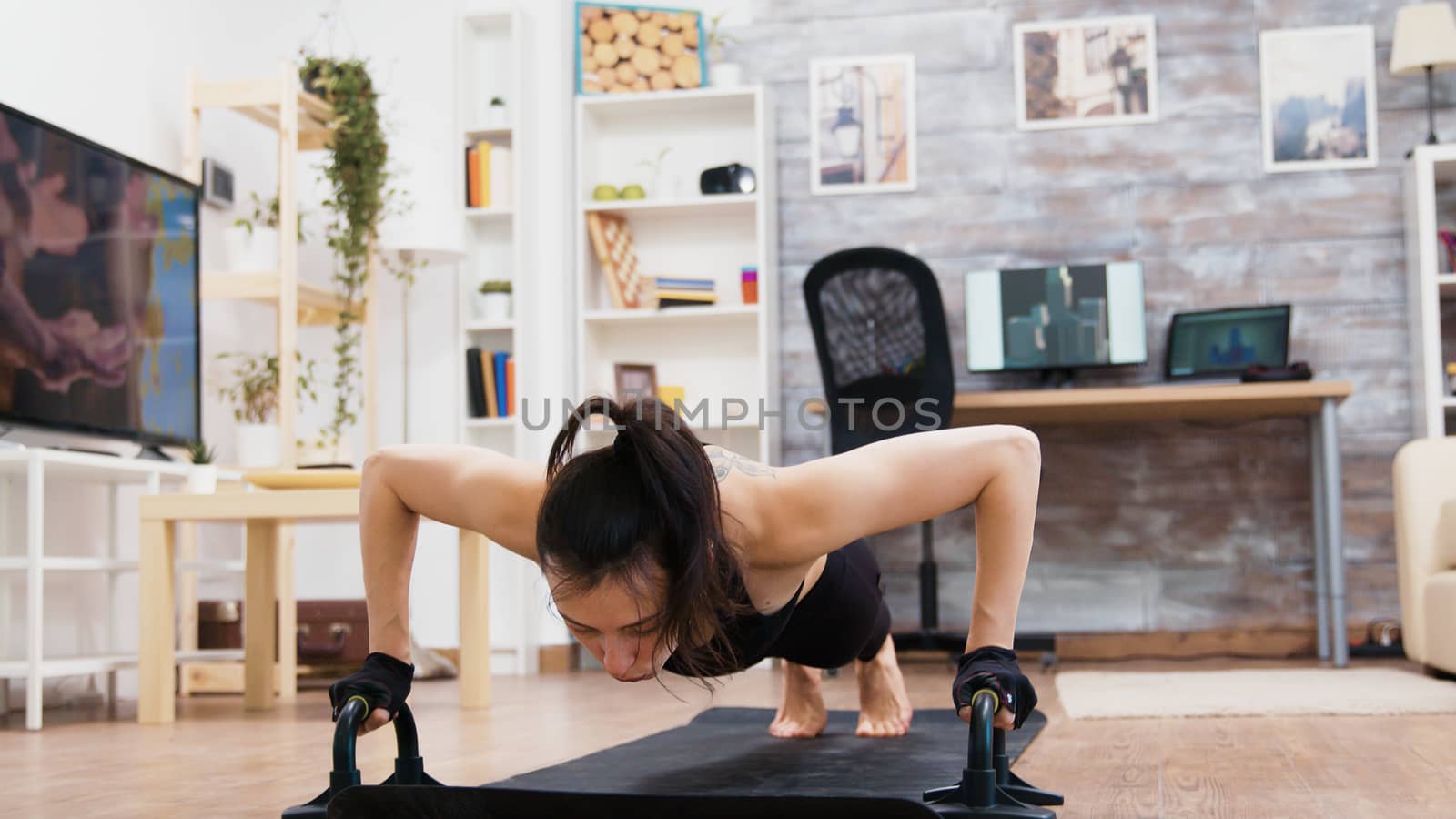 Young and strong woman doing push ups at home using push-up bars.