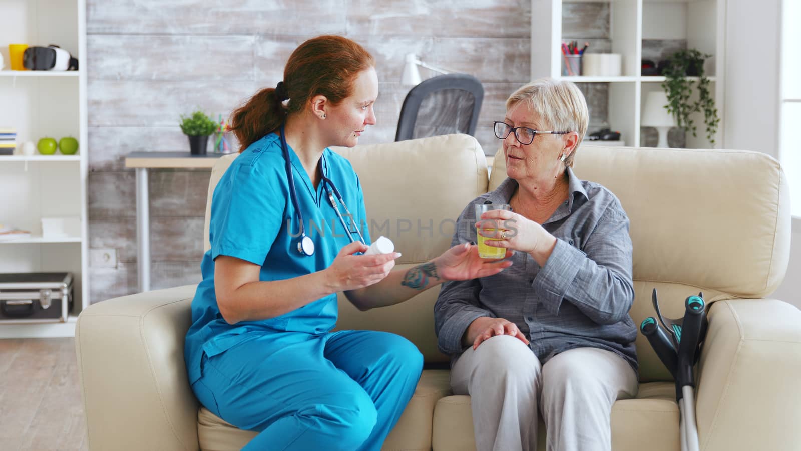 Female doctor sitting on sofa with senior woman in nursing home giving her daily pills.
