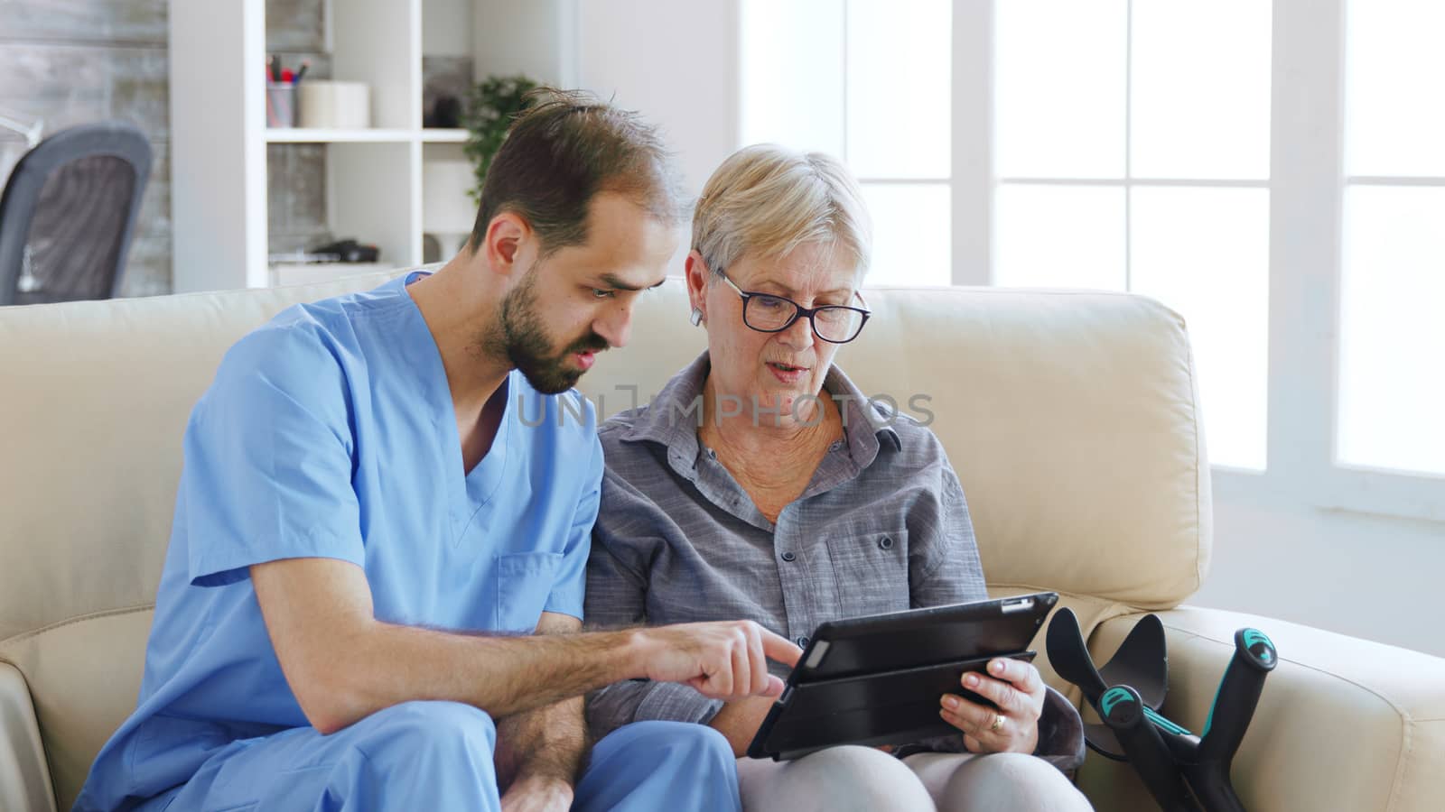 Male assistant teaching senior retired elderly old woman how to use her tablet computer by DCStudio