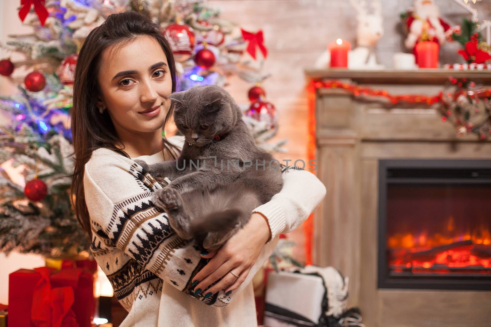 Happy young woman with her cat in front of fireplace celebrating christmas.