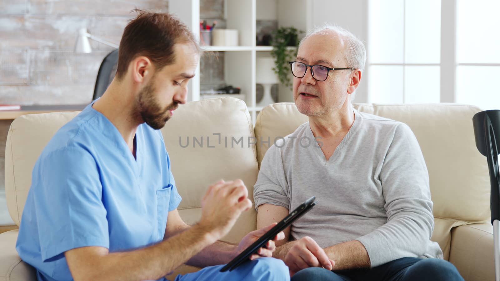 Caucasian male nurse talking with a nursing home patient about his health. The nurse is making notes on a digital tablet