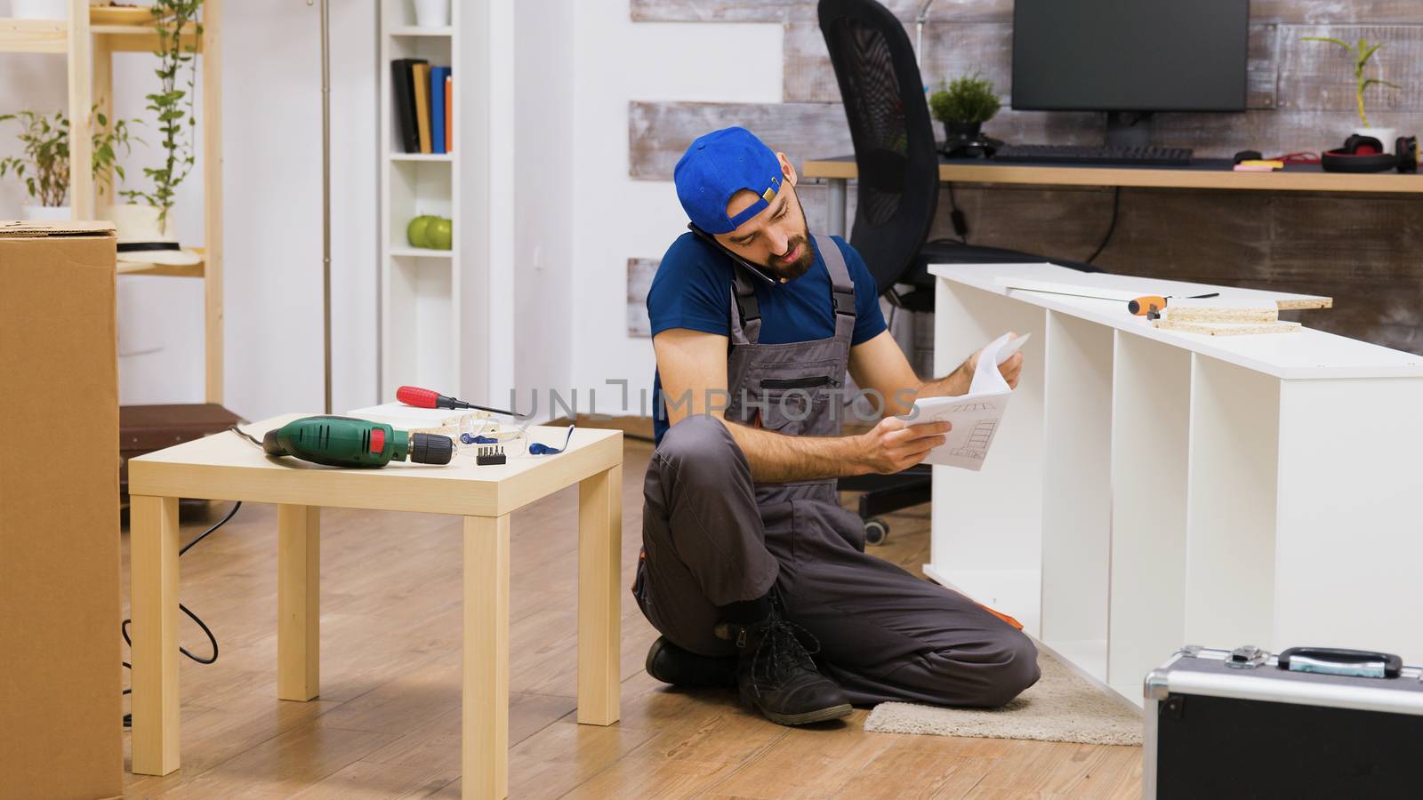 Male worker talking on the phone while assembles white furniture by DCStudio