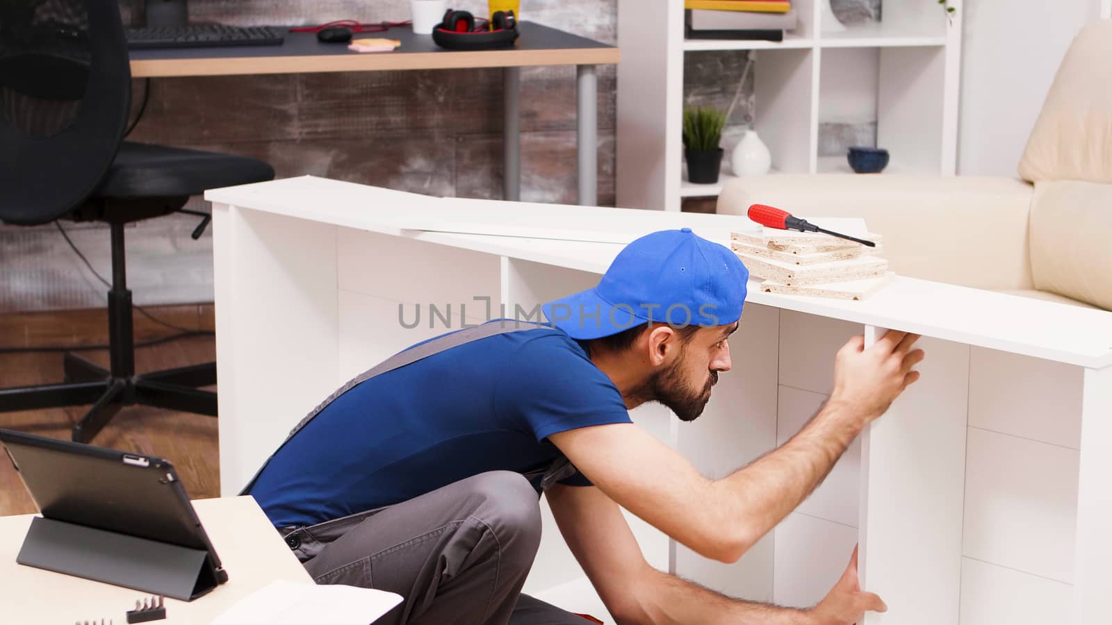 Attractive handyman assembles new furniture for home owners. Worker reading instructions from tablet computer.