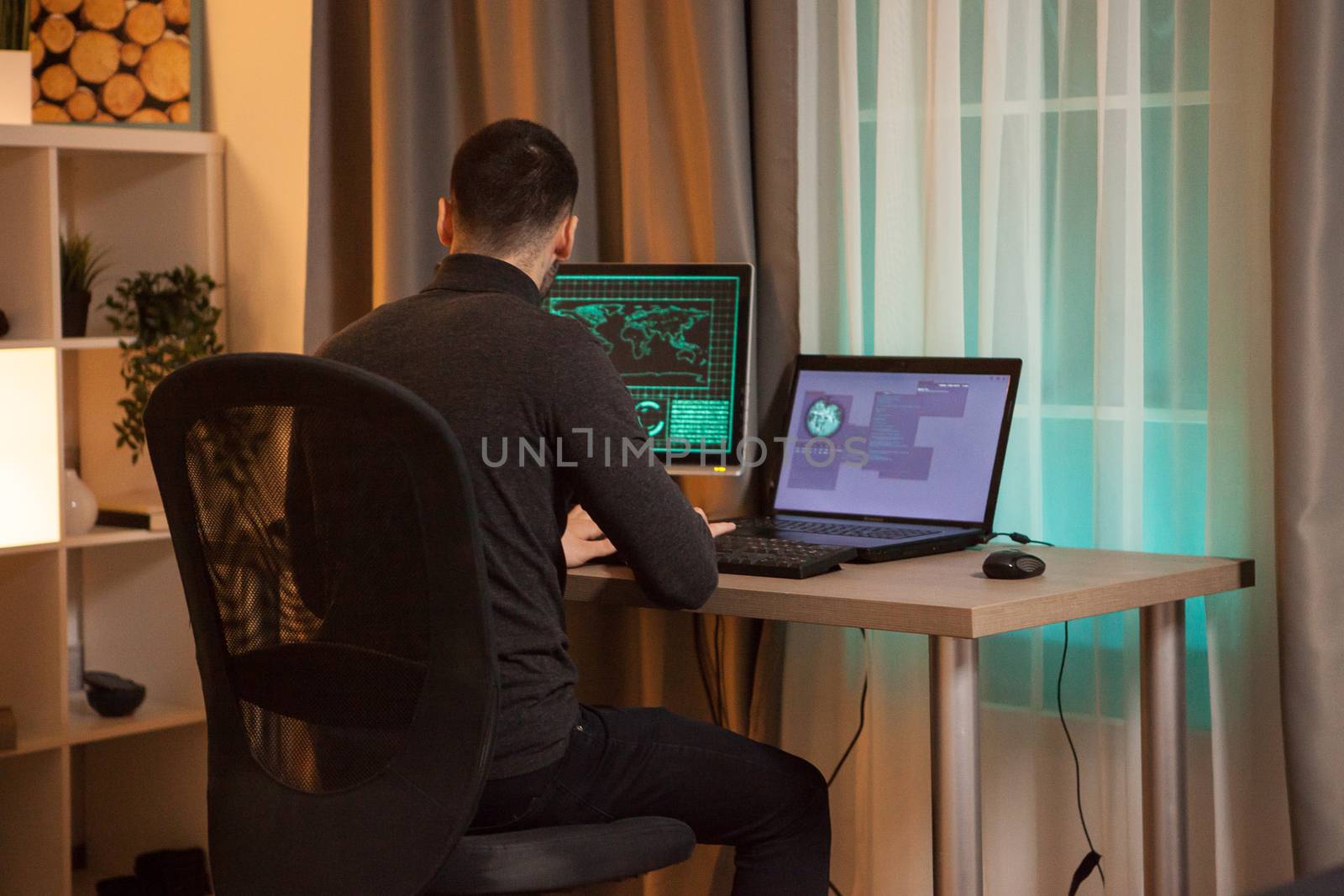 Back view of young hacker typing a virus on laptop at night time.