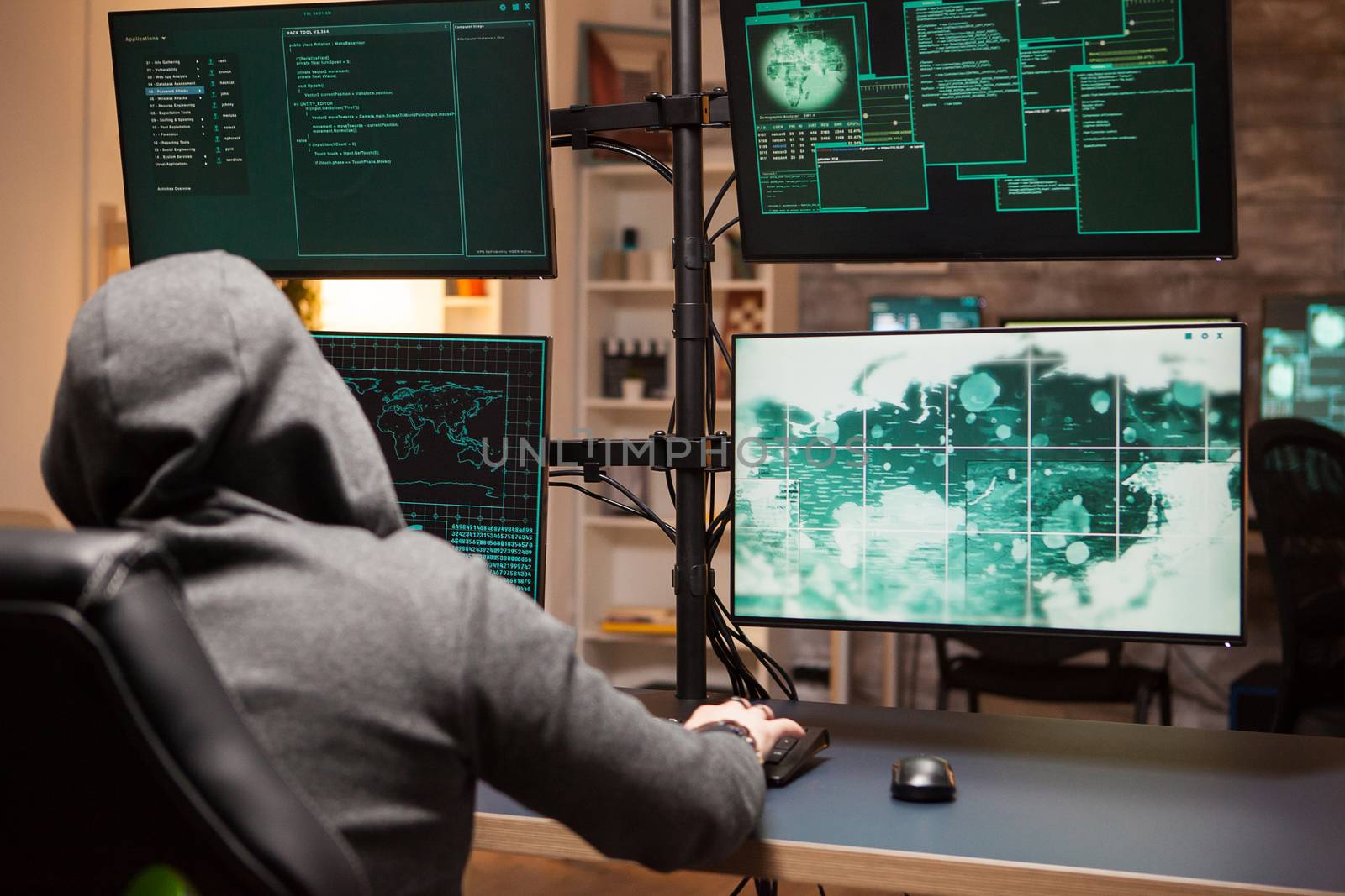 Cyber criminal wearing a hoodie writing a dangerous virus using computer with multiple screens.