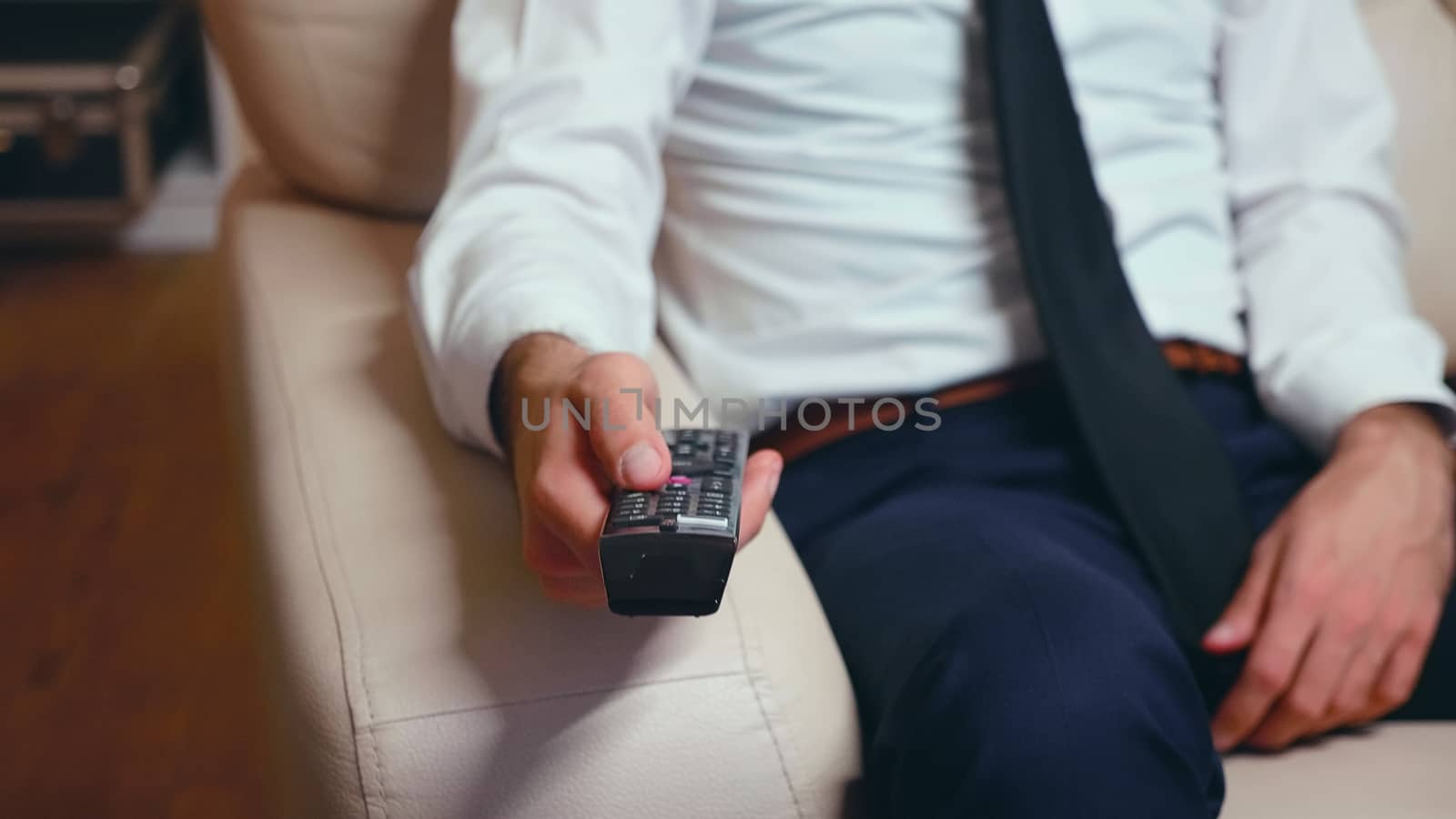 Businessman at home in formalwear and a tie resting and using tv remote control.