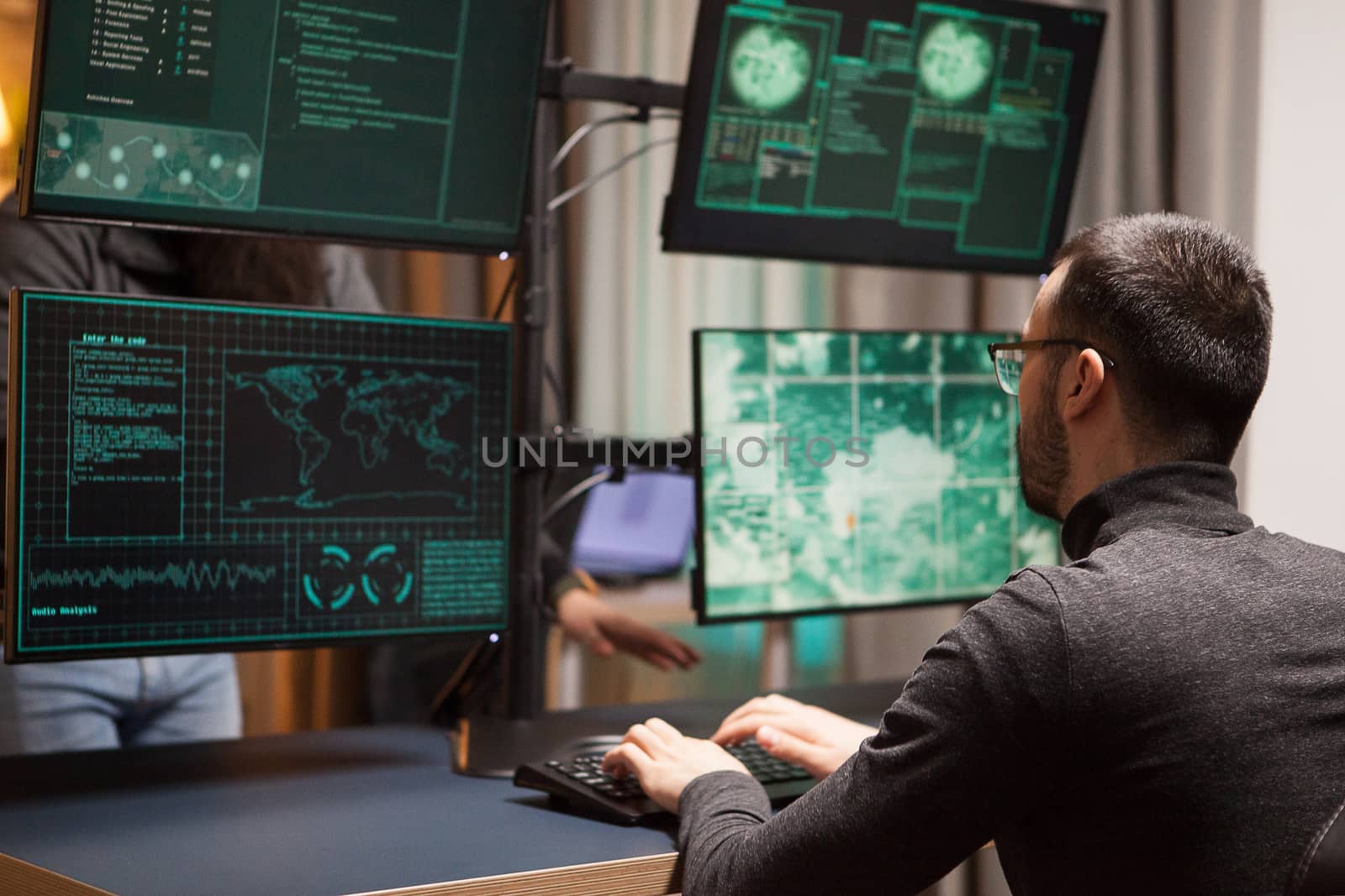 Young hacker making a dangerous virus for cyber attacks on computer with multiple screens.