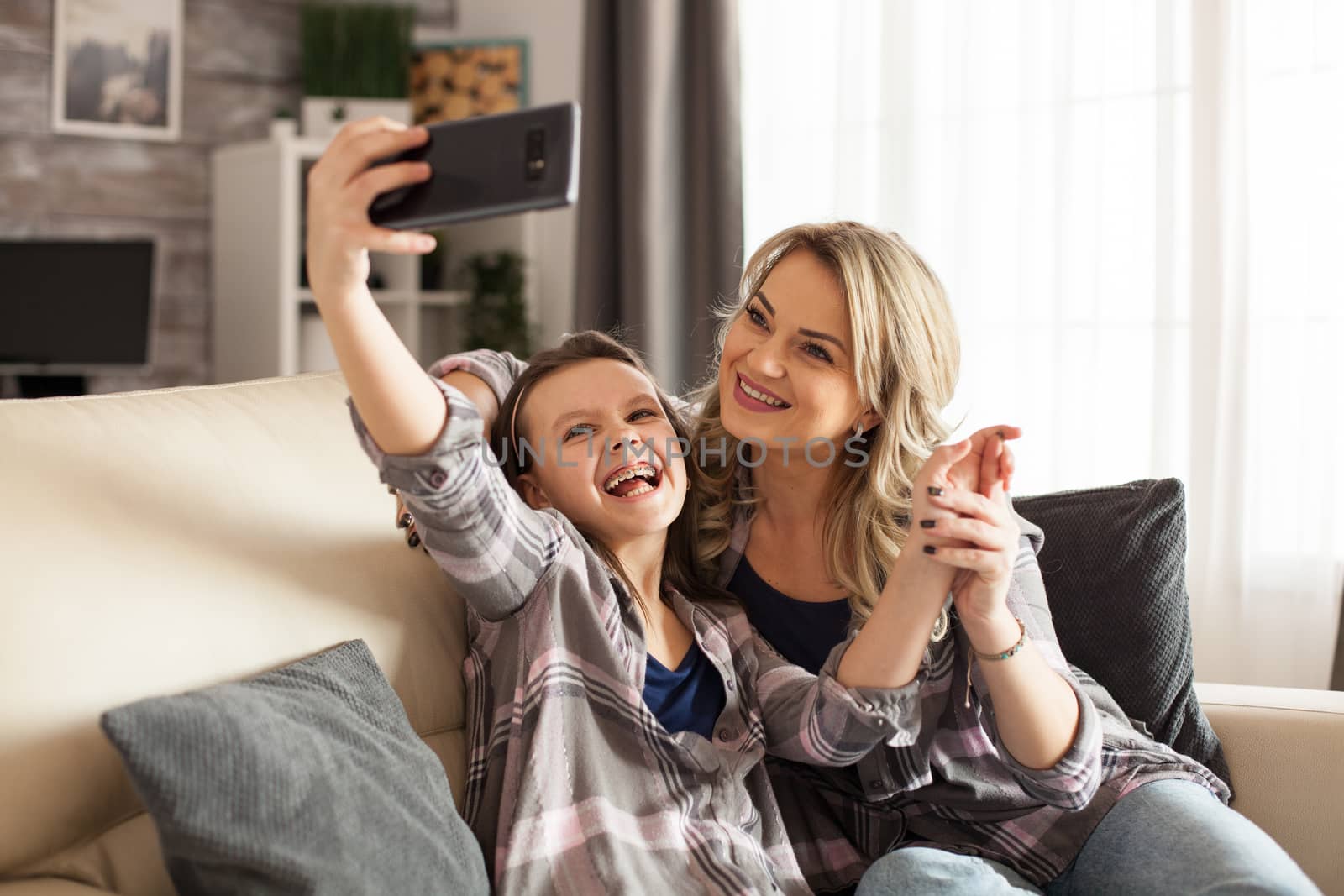 Mother and daughter laughing while taking a selfie on the couch in living room.