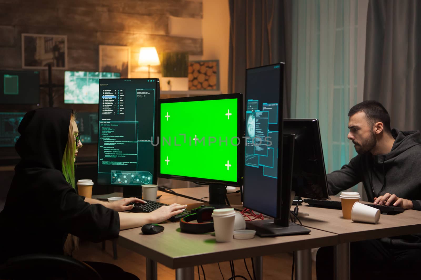 Female hacker with a hoodie in front of computer with green screen and male criminal.