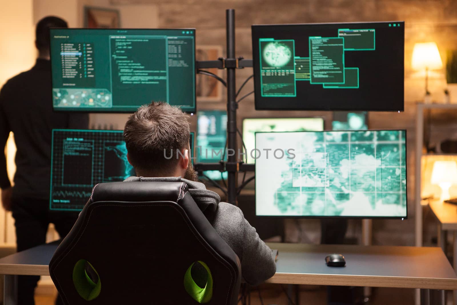 Rear view of hacker in front of computer with multiple screens by DCStudio
