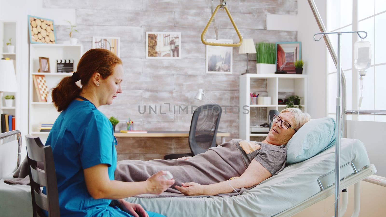 Caucasian nurse showing an old lady the pills dosage she supposed to take while she is lying in hospital bed in a retiremend home