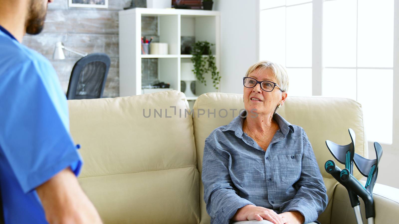 Senior old woman sitting on couch in nursing home talking with the doctor. Over the shoulder shot