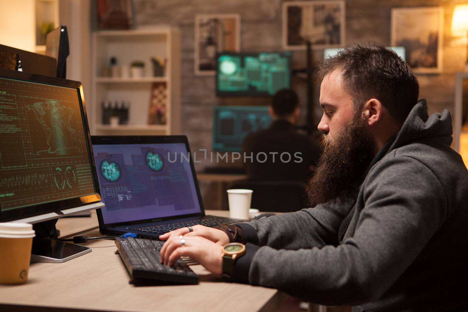 Adult hacker typing a virus on computer to break firewall security. Young hacker in the background.