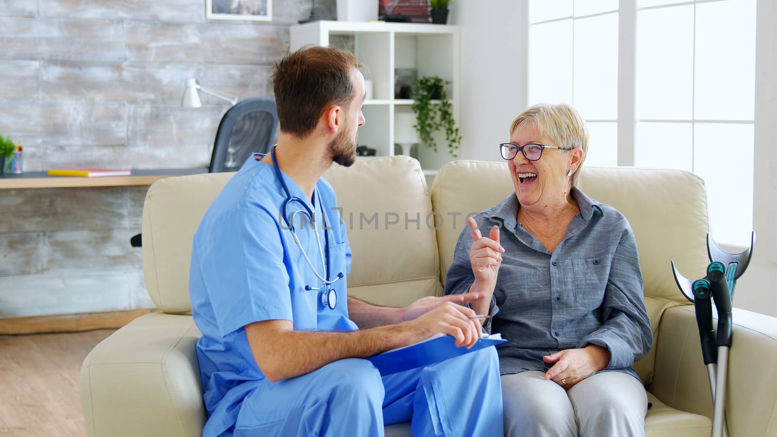 Doctor assistant taking notes on clipboard while listening to old retired woman in nursing home. Caregiver and social worker