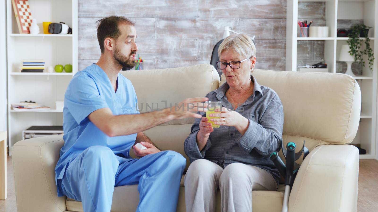 Male nurse sitting on couch with senior woman giving her medical treatment in nursing home.