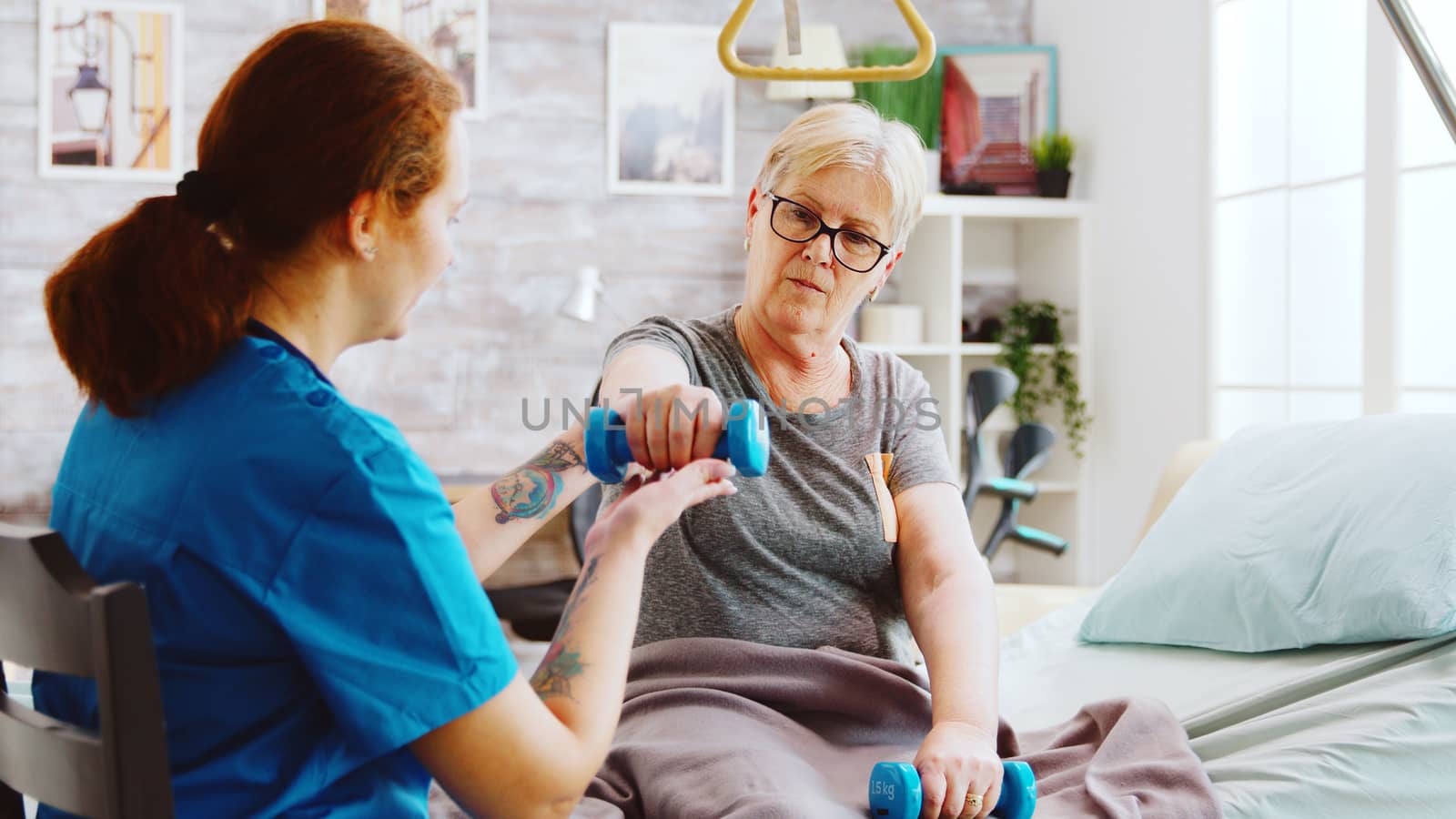 Revealing shot of female nurse helping an elderly woman to recover her muscles by DCStudio