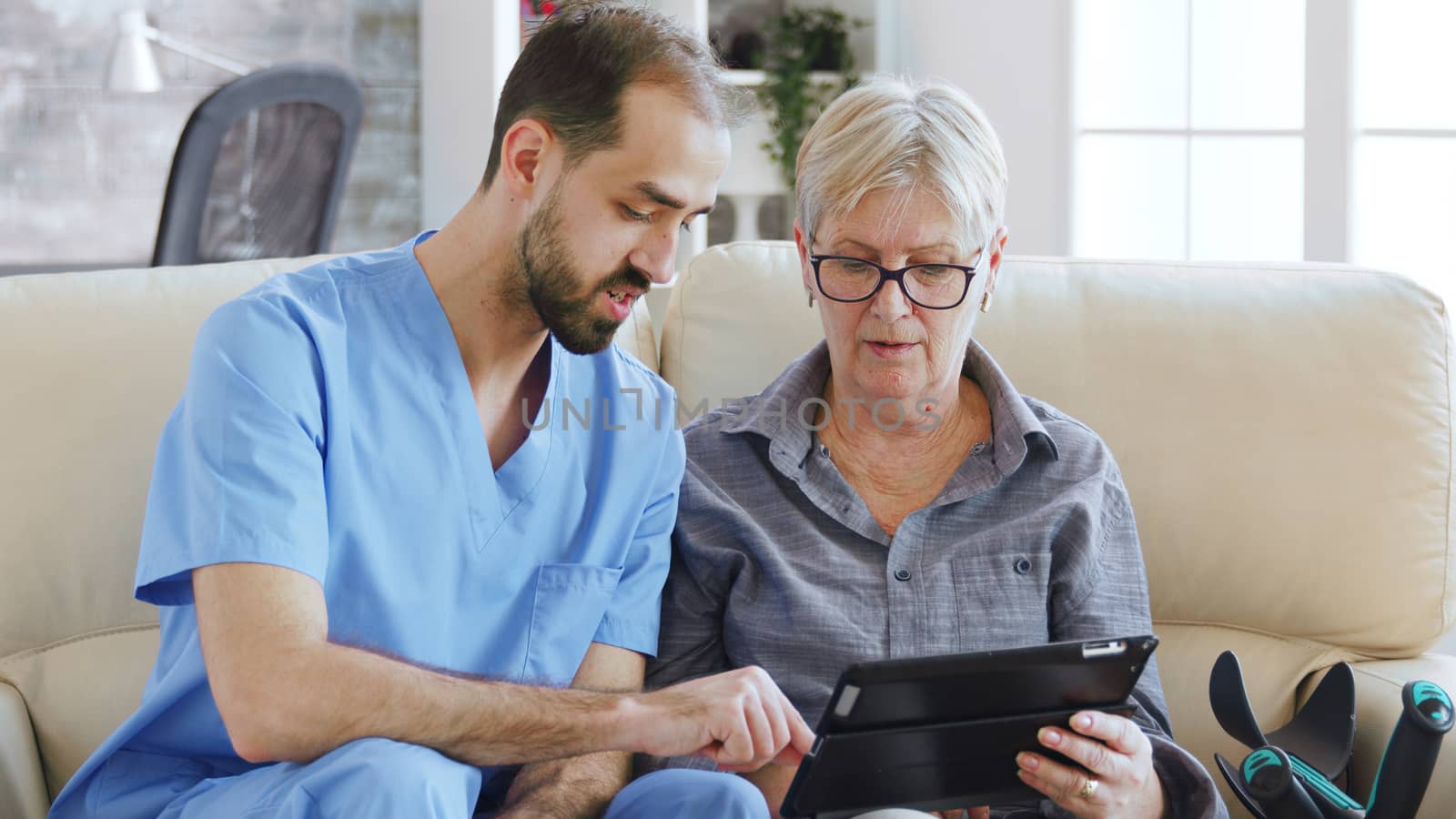 Male assistant teaching senior retired elderly old woman how to use her tablet computer by DCStudio