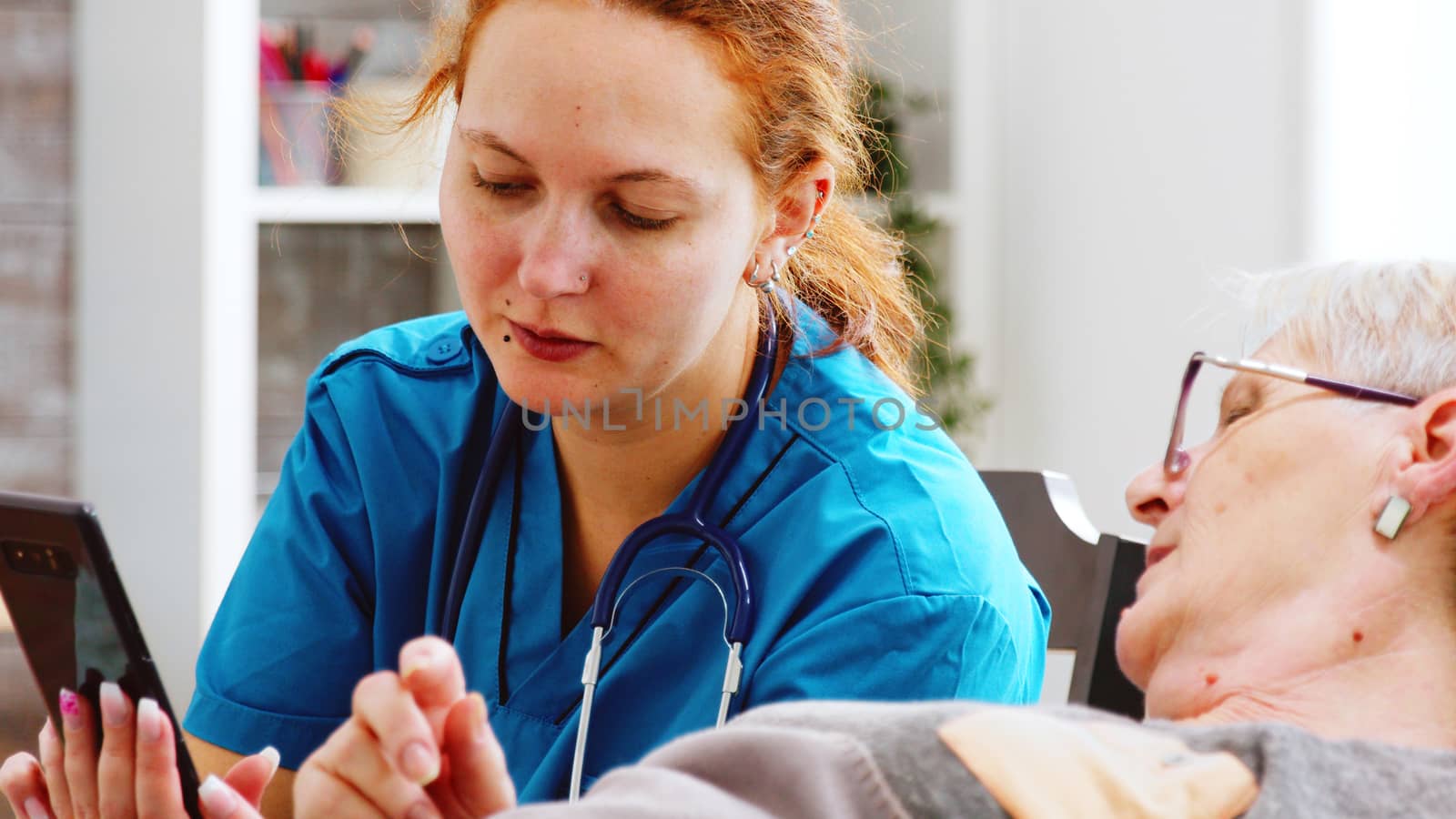 Close up shot of nurse helping an elderly disabled woman to use a smartphone by DCStudio