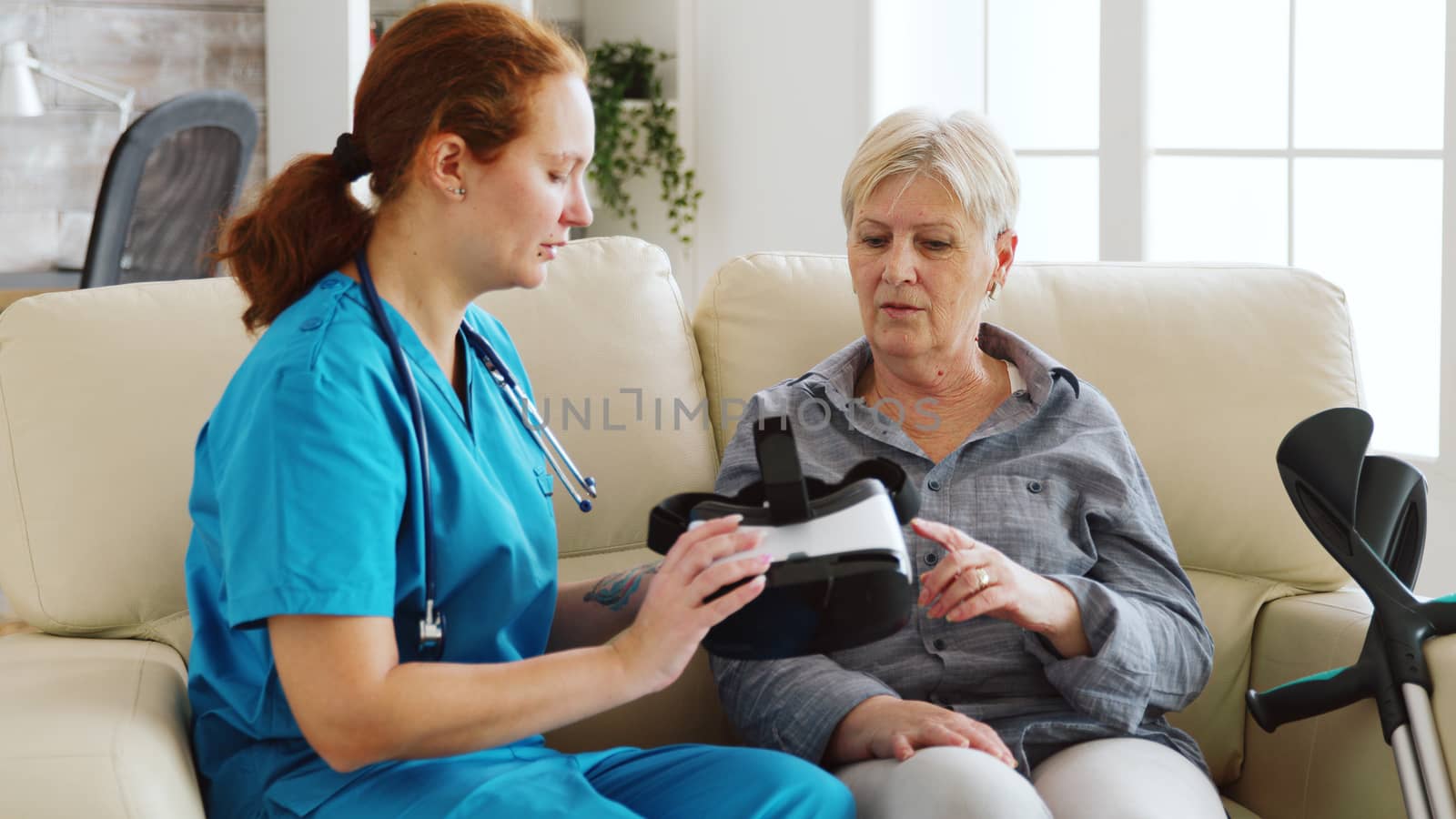 Female nurse helping senior woman to experience virtual reality with vr goggles in nursing home