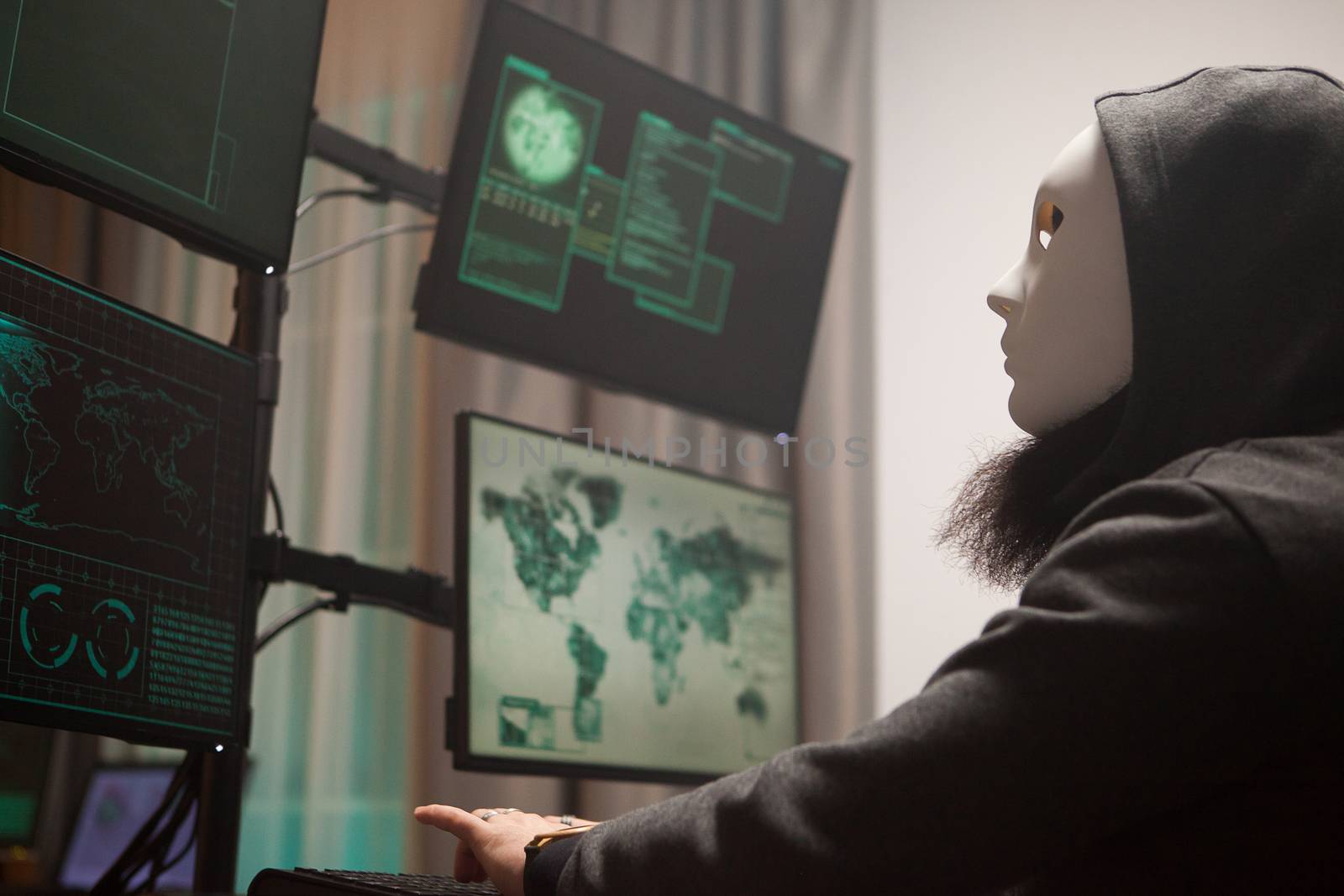 Masked hacker with a hoodie using computer to plan a massive cyber attack against gouvernements all over the world.