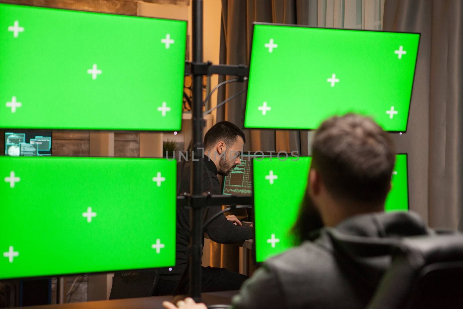 Focused young hacker making a dangerous malware on computer with green screens.