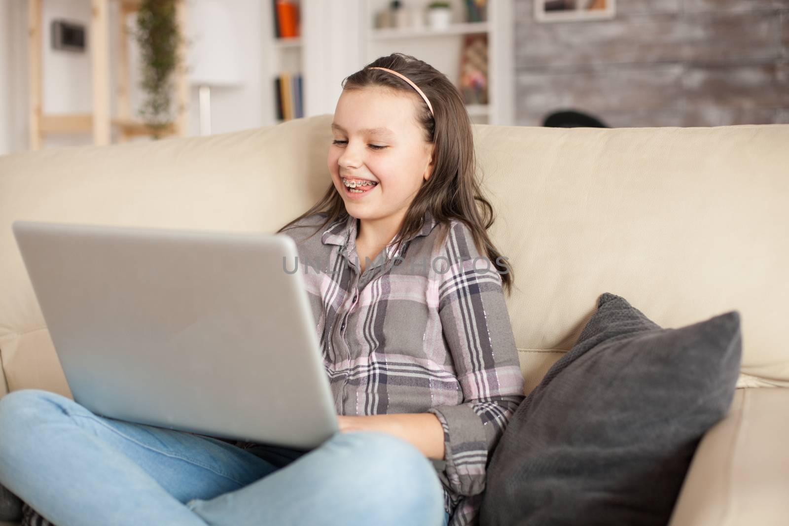 Smiling little girl with braces using her laptop in living room. Cheerful child.