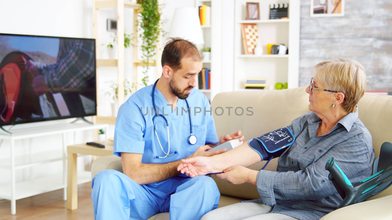 Bearded doctor in nursing home taking the blood pressure of senior woman in nursing home