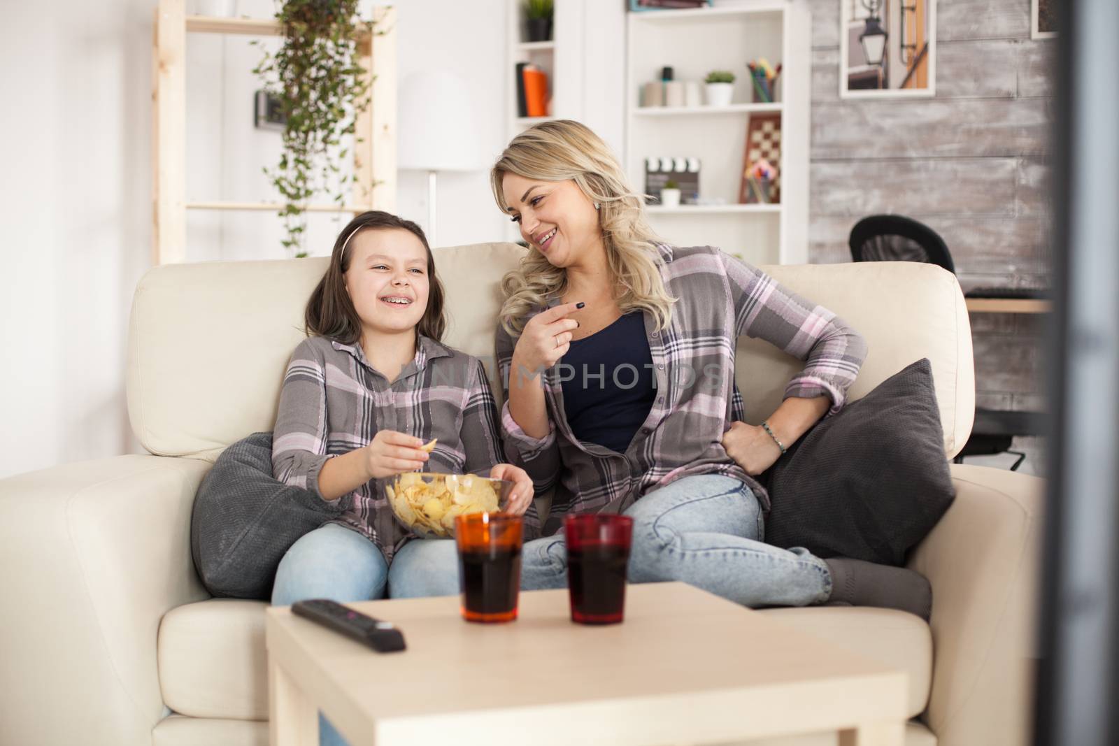 Little girl and her mother laughing while watching tv by DCStudio