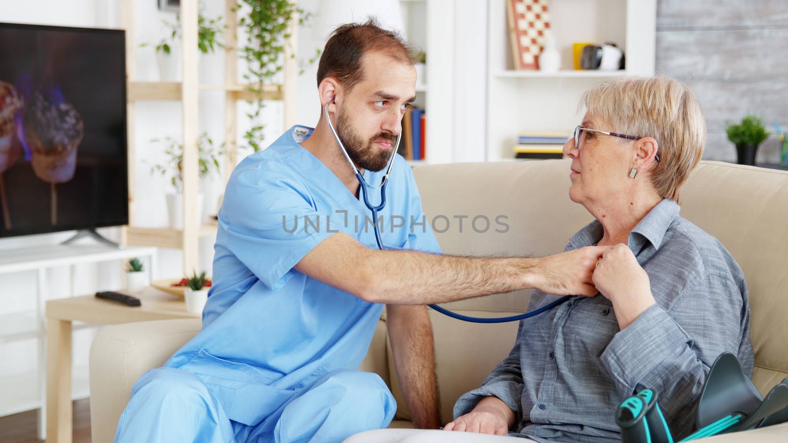 Male doctor putting his stethoscope on and listening old woman heartbeat by DCStudio