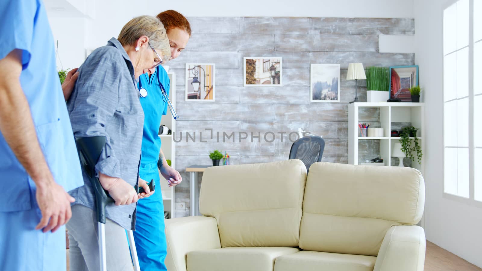 Nurse team helping old disabled lady to walk in the nursing home room. Caregiver and social worker