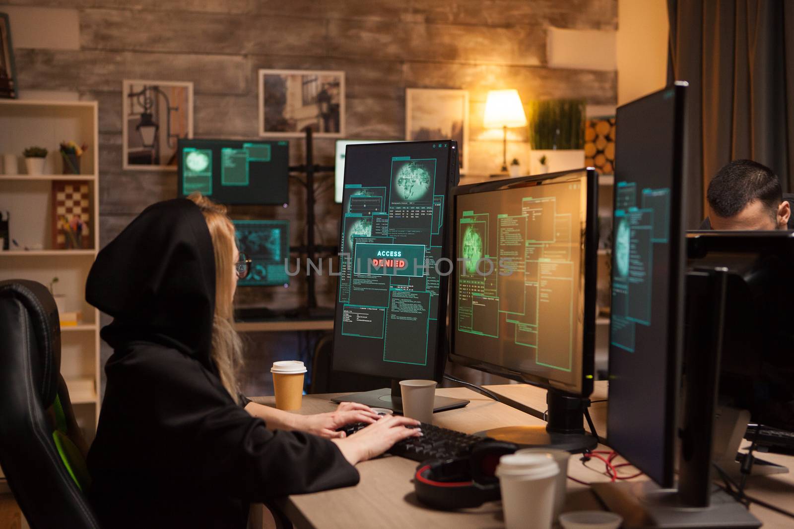 Side view of female hacker wearing a hoodie to cover her face while stealing information from a firewall.
