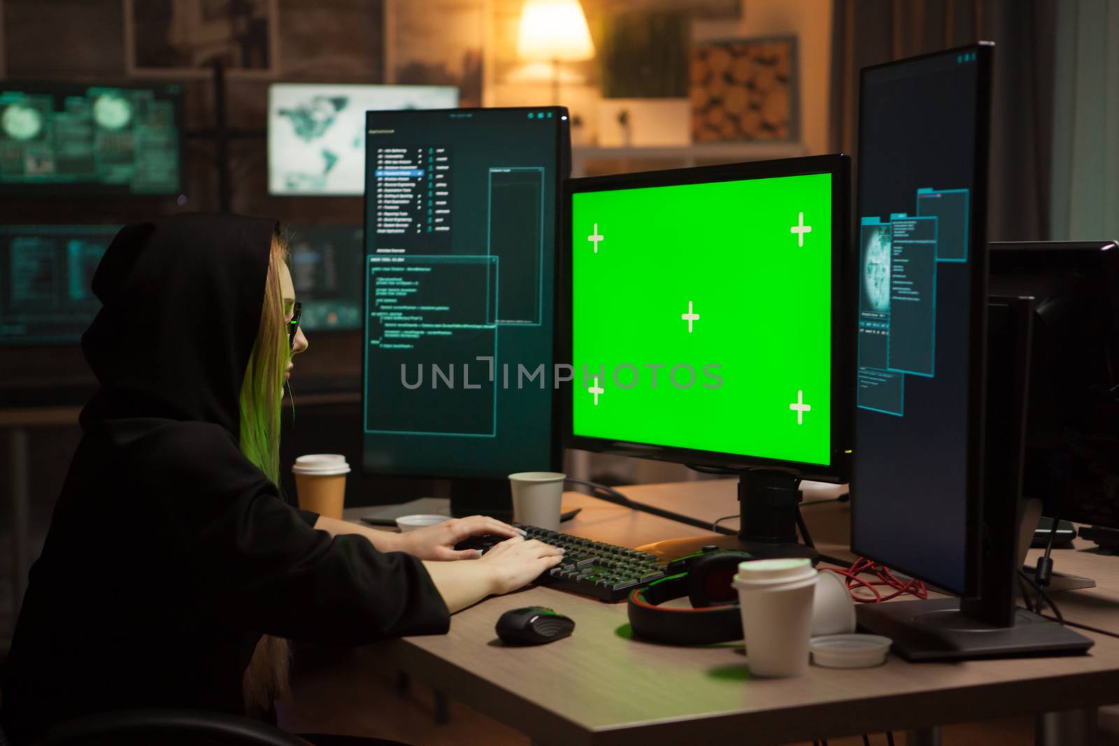 Female cyber criminal typing on computer with green screen. Corporate hacking.