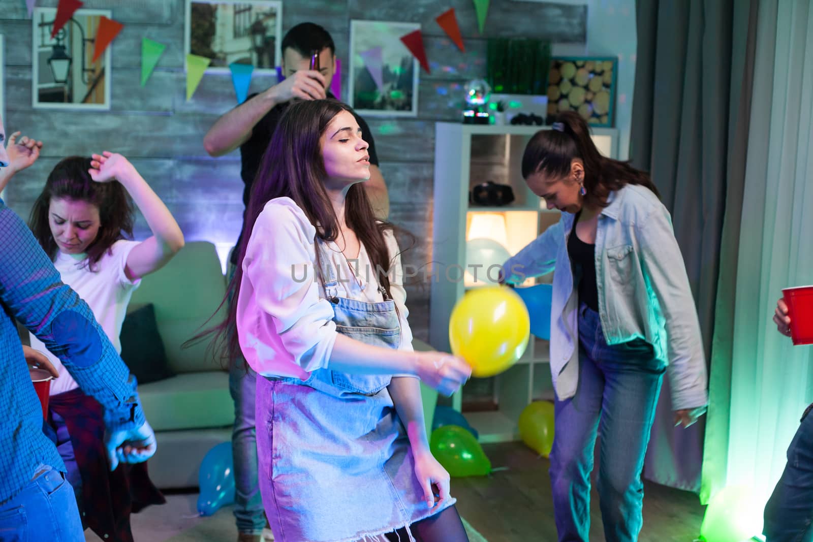 Beautiful young woman holding a balloon while dancing at a party with her friends.