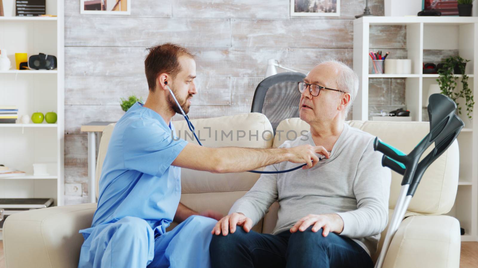 Revealing shot of young male nurse listening to old retired man heartbeat by DCStudio