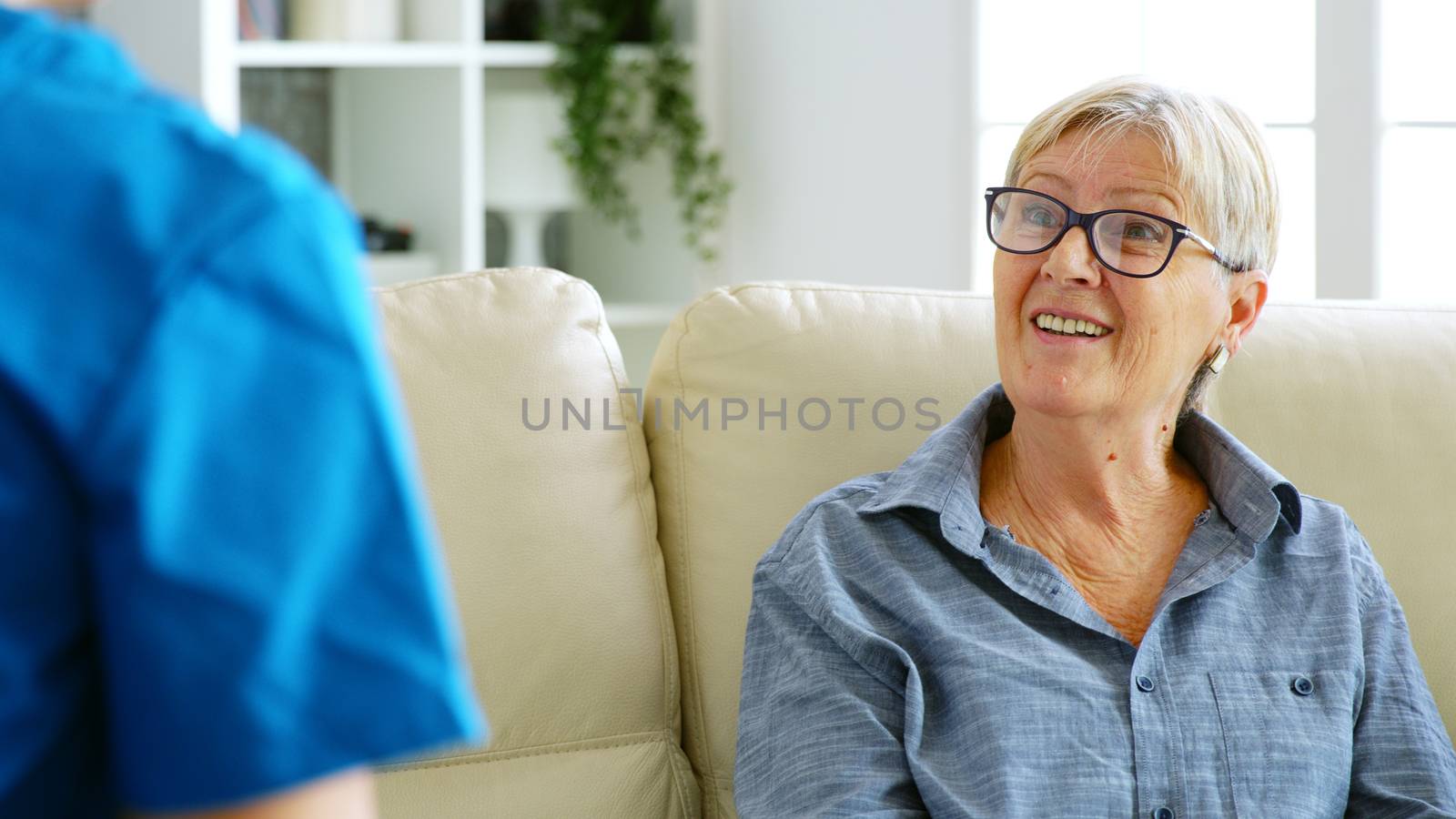 Senior old woman sitting on couch in nursing home talking with the doctor. Over the shoulder shot