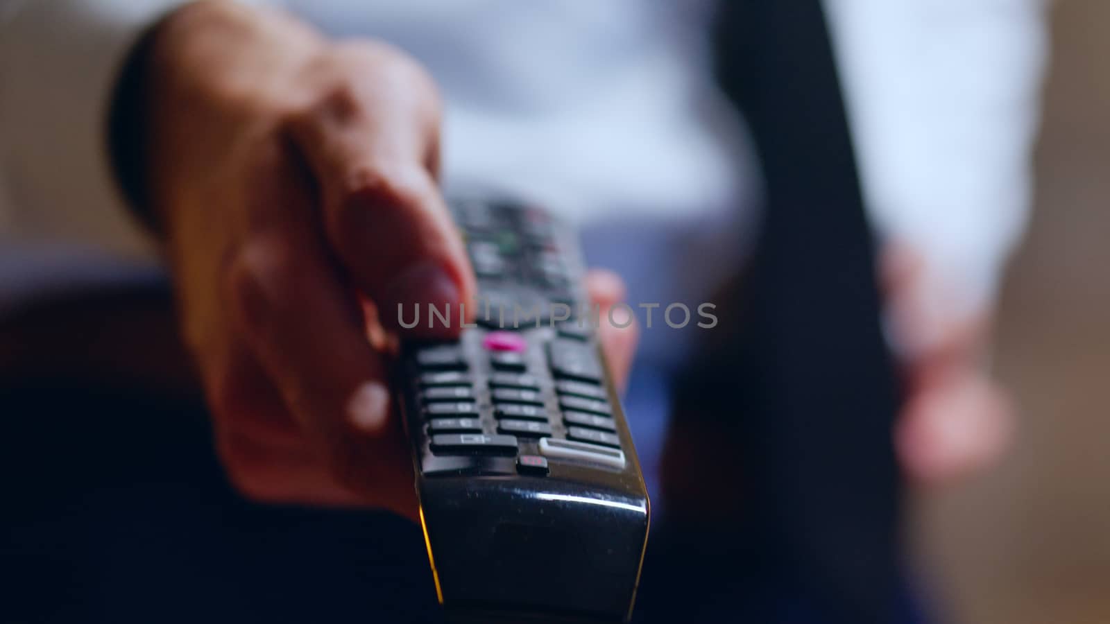 Close up of businessman relaxing after work using tv remote control switching channels.