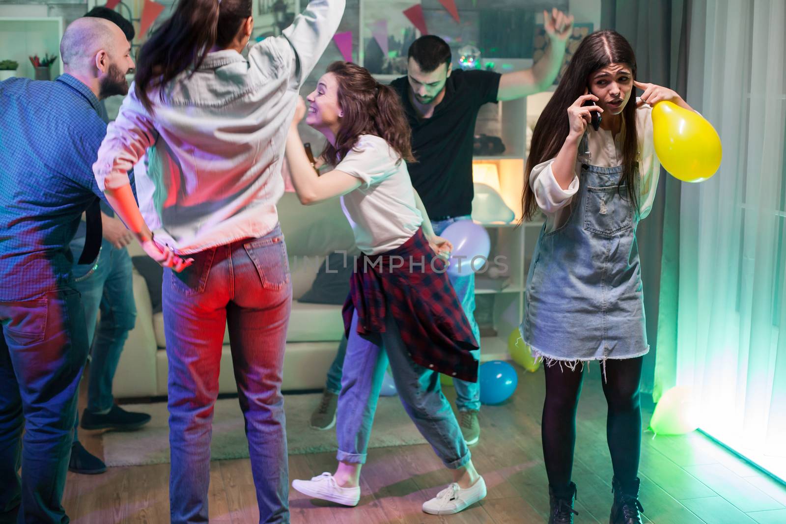 Group of young people dancing at a party while girl trying to have a conversation on her phone.
