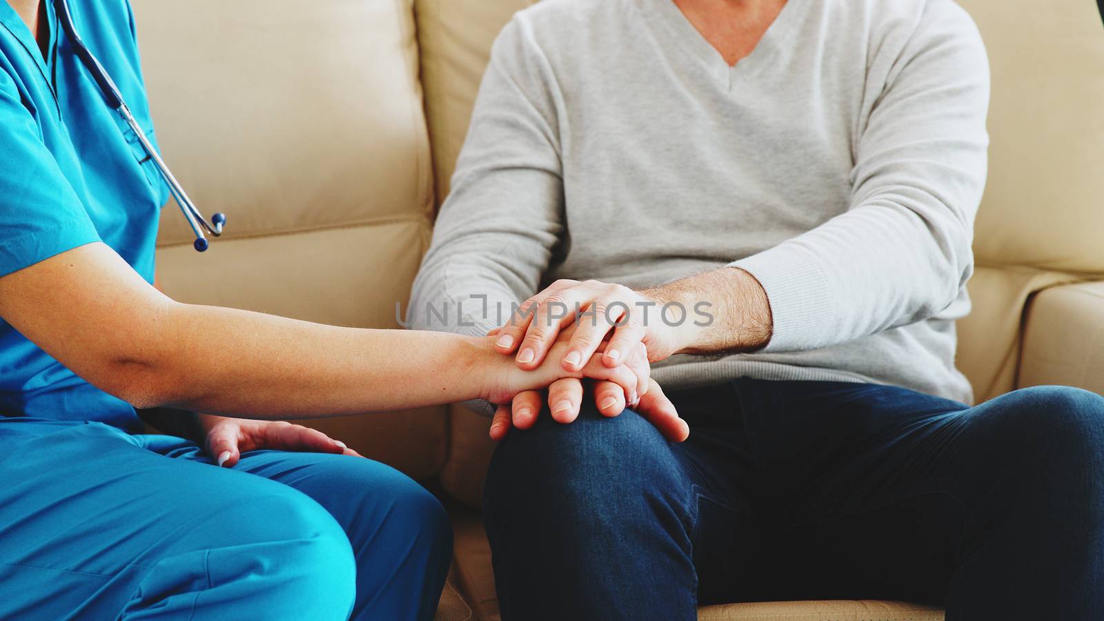 Slow motion close up shot of female nurse taking an old man hand while they are sitting on the couch in nursing home. Caregiver and social worker