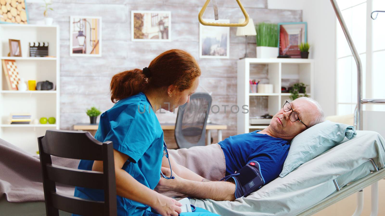 Female nurse checking old sick man blood pressure. The elderly man lies in a hospital bed in a bright and cozy nursing retirement home