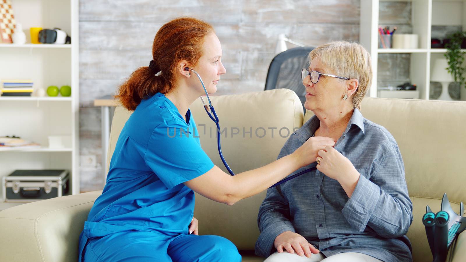 Caucasian female doctor in nursing home listening old woman heartbeat with stethoscope