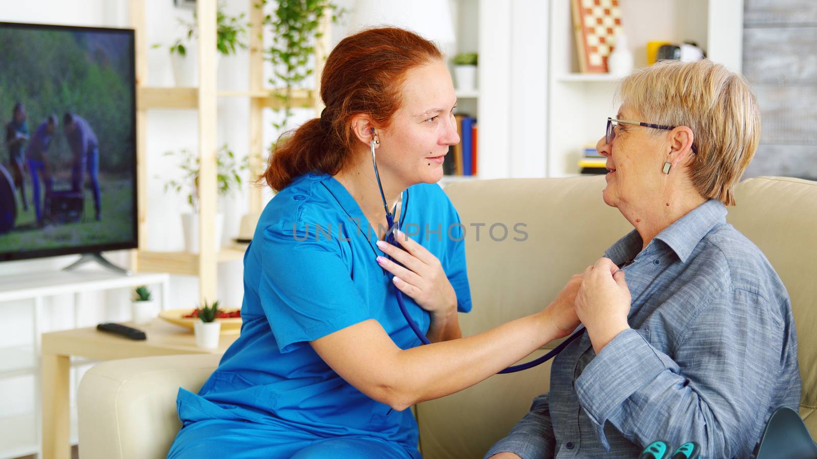 Caucasian female doctor in nursing home listening old woman heartbeat with stethoscope