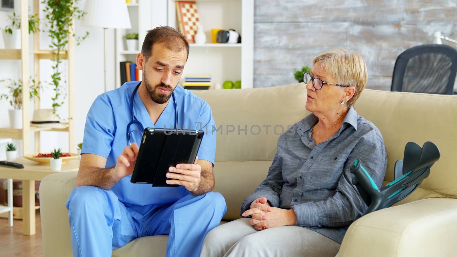 Doctor assistant taking notes on clipboard while listening to old retired woman in nursing home. Caregiver and social worker