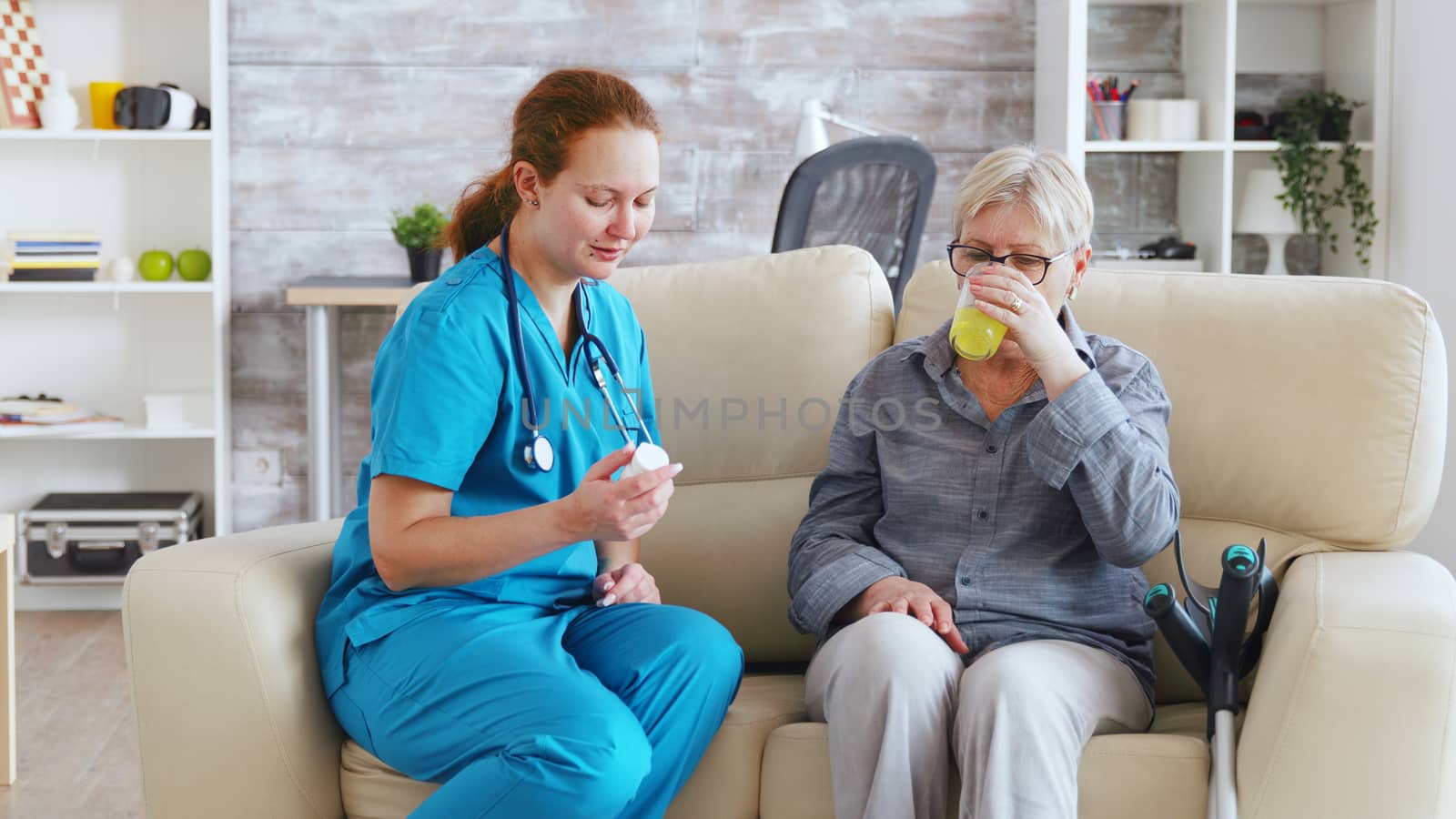 Female doctor sitting on sofa with senior woman in nursing home giving her daily pills by DCStudio