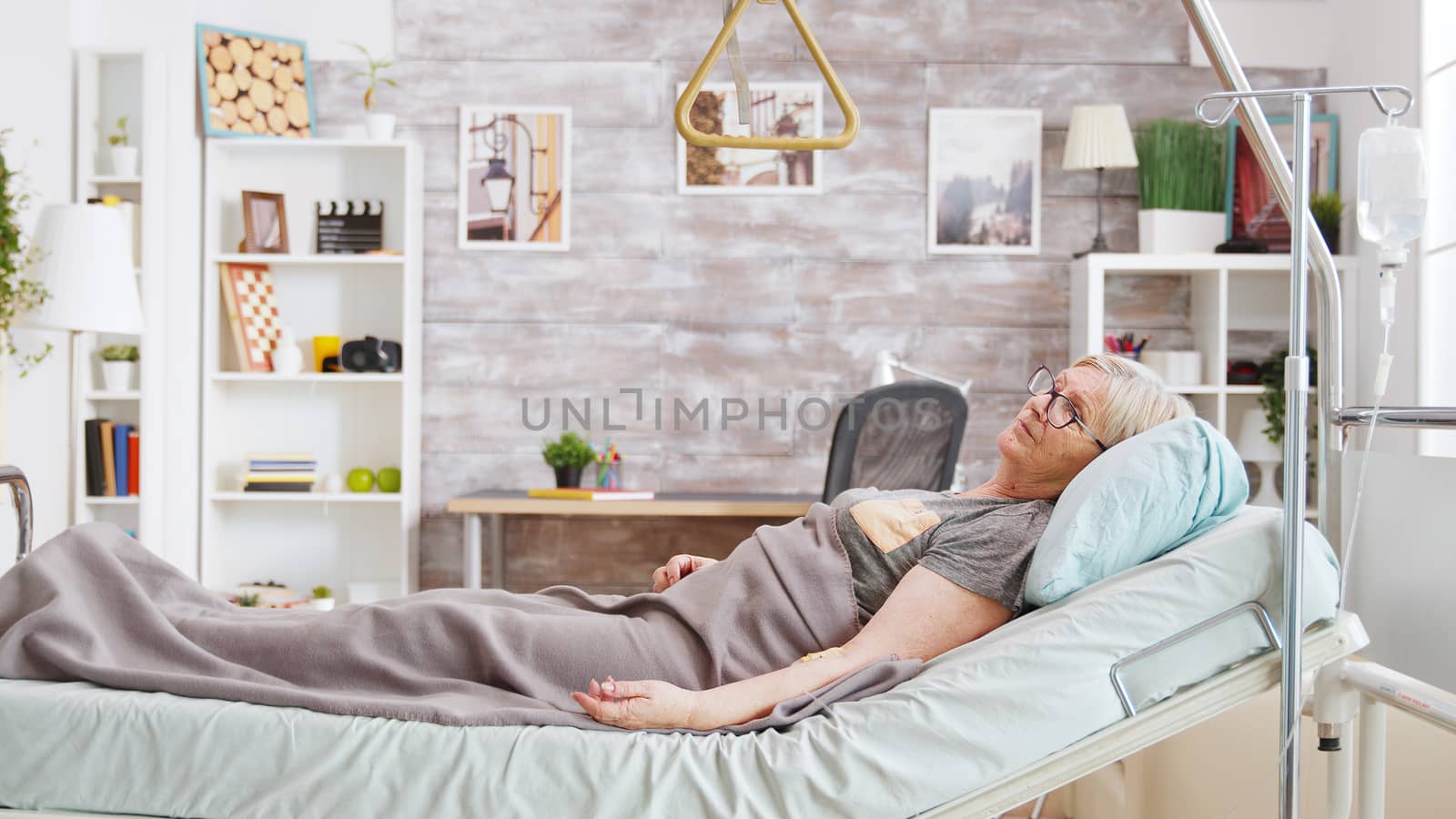 Retired disabled lady lying in hospital bed in cozy and bright room in retirement home.