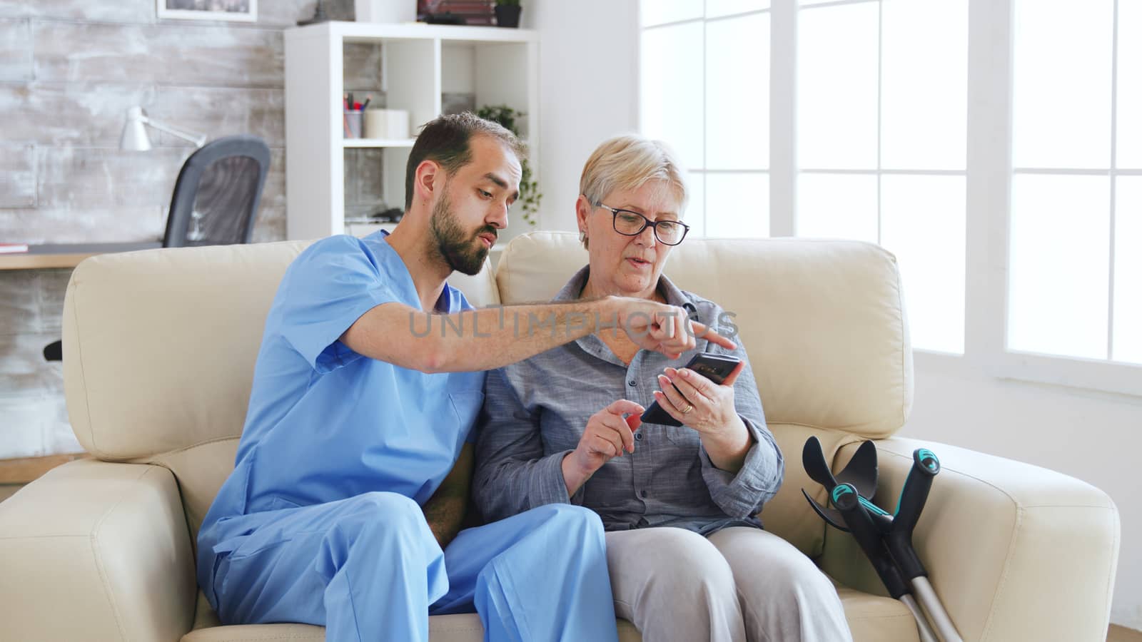 Male doctor teaching senior woman how to use her phone in nursing home