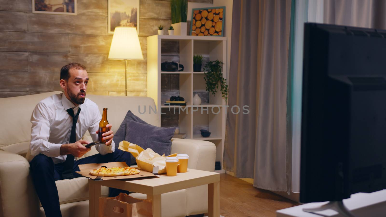 Businessman with tie arriving at home with pizza after work. Beer in front of tv.