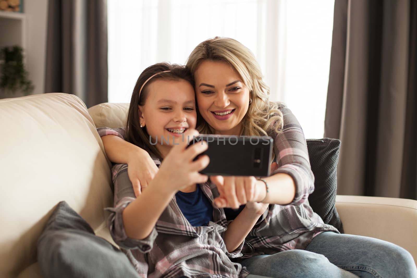 Mother and daughter sitting on the couch in living room browsing on the phone.