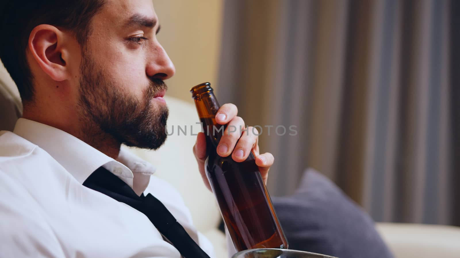 Side view of businessman drinking beer after work in his apartment.